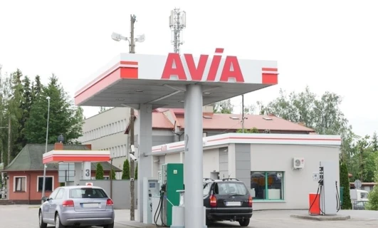 Samochód rodzinny zaparkowany przy stacji paliw z dystrybutorem paliwa w tle. Bumper, lusterka i tablica rejestracyjna pojazdu są widoczne. Loga AVIA i SD Eibar również są obecne.